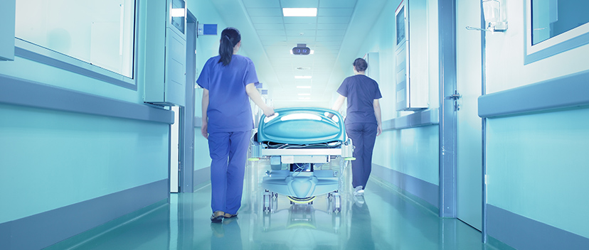 Two nurses walking down a hallway with a stretcher after a hospital room has been cleaned