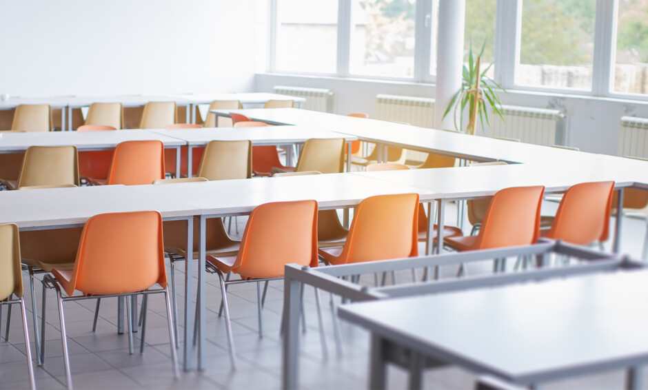 Classroom with clean white tables and orange chairs, highlighting the importance of maintaining clean learning environments in schools and universities