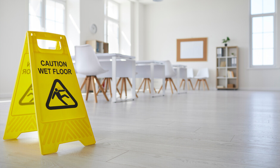 Yellow “Caution Wet Floor” sign placed in a clean, modern classroom or meeting space with white chairs and desks.