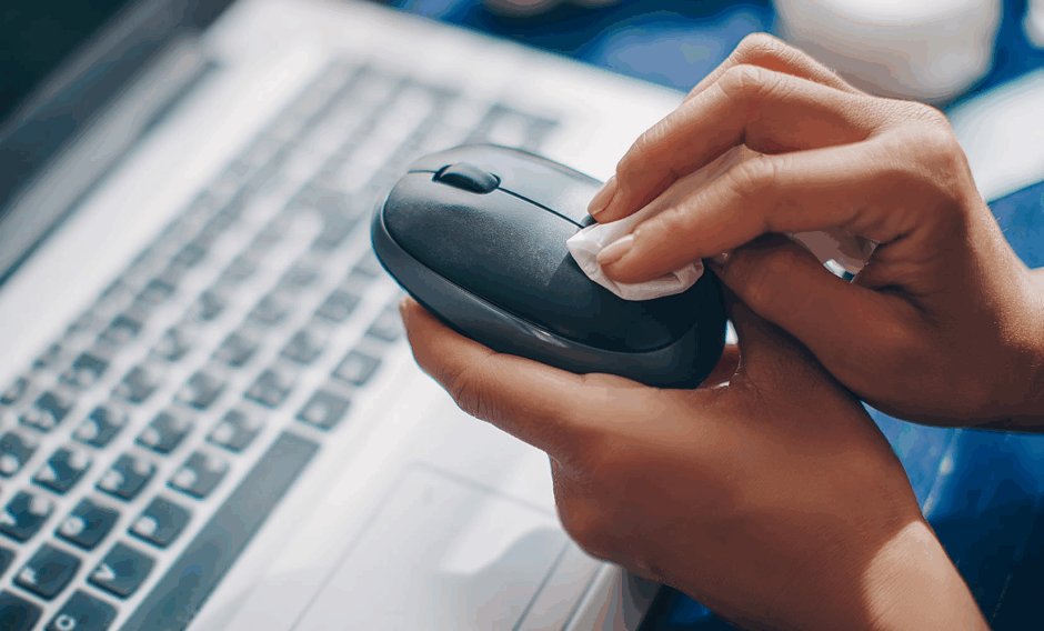 Up close photo of hands wiping a computer mouse and laptop to represent disinfection awareness